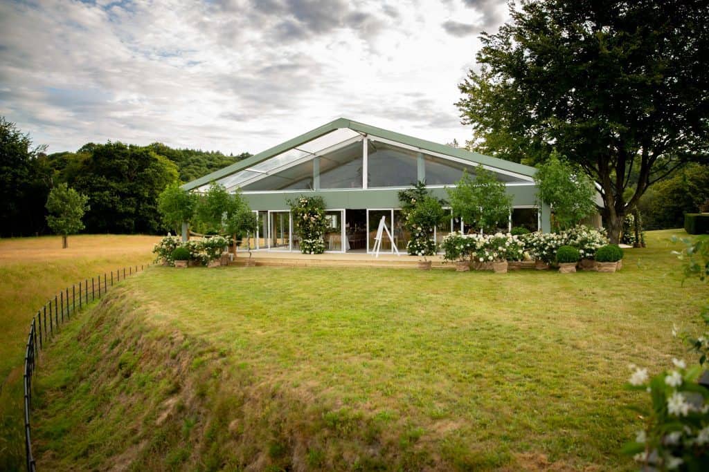 A marquee on a lawn viewed from outside, surrounded by trees and foliage. Clearspan marquee hire. Marquees